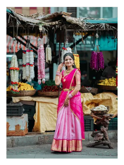 A full-length shot of the bride-to-be in her pink saree, standing gracefully amidst the colors of a local flower market.