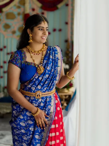 A bride in a stunning blue and red silk saree, captured in a moment of quiet reflection.