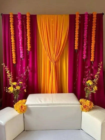 A simple yet elegant backdrop for a Haldi or Mehendi ceremony at home. We used vibrant drapes in pink and orange with marigold flower strings to create a traditional and cheerful look.