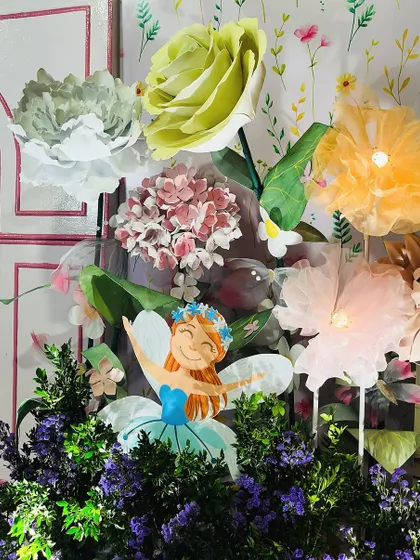 A close-up of the whimsical details in a fairytale party. Here, a cheerful fairy cutout is nestled among oversized paper flowers, adding a playful and artistic touch to the floral arrangements.