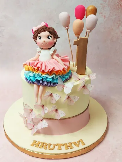 We celebrate a first birthday with this enchanting princess butterfly cake. A sweet fondant girl in a rainbow tutu sits atop the cake, which is adorned with fluttering butterflies and a bouquet of balloons, creating a scene of pure childhood magic.