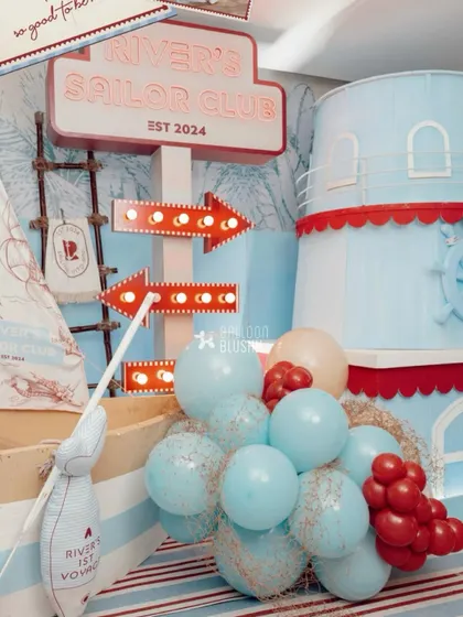 A detailed shot of the party entrance, with a large 'River's Sailor Club' sign, light-up arrows, and a cascade of balloons.
