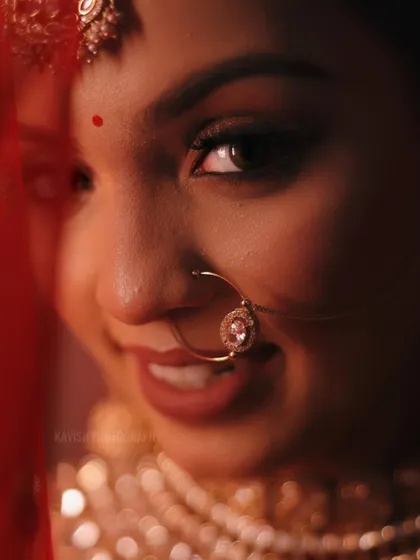A playful and intimate bridal portrait taken through her red veil. The focus is on her joyful expression and the details of her nose ring.
