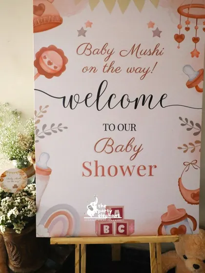 A full view of the personalized welcome sign for the 'Baby Mushi' baby shower, designed with cute baby-themed illustrations and set on a wooden easel.