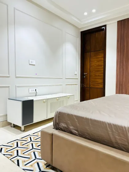 A minimalist bedroom design with clean white walls featuring classic molding. The geometric rug adds a pop of pattern and visual interest to the floor.