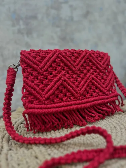 A side view of the red sling bag, showing the texture of the knots and the fringe.