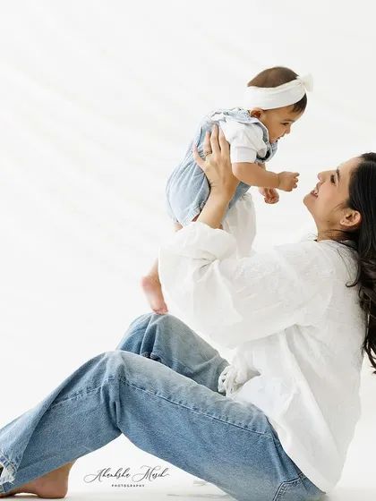 The simple joy of a mother and her baby. Dressed in casual whites and jeans, their relaxed smiles and easy connection shine in this bright, airy portrait.