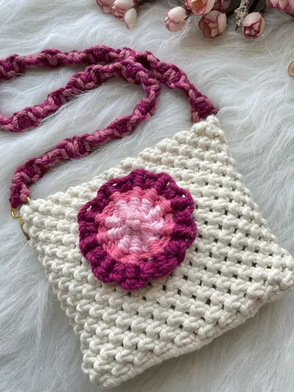 A simple off-white sling bag made special with a multi-toned pink and magenta floral appliqué. The braided strap adds another layer of texture and color.