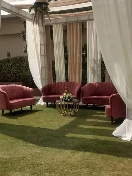 An intimate and elegant lounge corner created with plush scalloped velvet sofas in a deep rose color. This setup, placed under a draped canopy on the lawn, offers a private space for conversation.