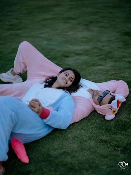 The couple lies on the grass in their onesies, sharing a quiet, sweet moment and looking up at the sky.