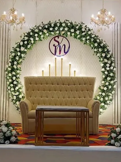 A chic and modern stage design with a white circular floral wreath and monogram. The ribbed white backdrop and high-back sofa create a clean and sophisticated look.