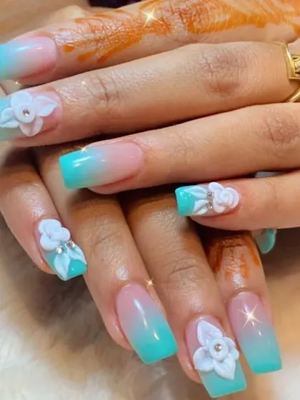 A stunning set of turquoise ombre nails on a square shape, beautifully decorated with intricate 3D white flowers.