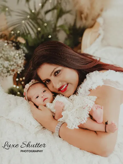A beautiful mother-daughter portrait. The mother is smiling at the camera while holding her newborn, who is looking right back at her.