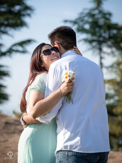 A joyful embrace from behind, with her holding a small bouquet of wildflowers. This shot captures a spontaneous and loving moment.