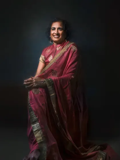 This full-length portrait showcases the elegant drape of a pink sari. The lighting creates a dramatic, artistic effect that emphasizes both the subject's poised demeanor and the beauty of the traditional garment.