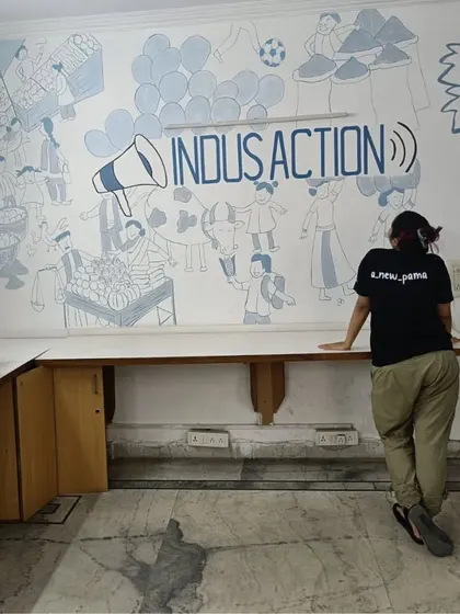 Standing in front of the completed mural project for Indus Action's office. The wall depicts the communities they serve, bringing the heart of their work into their daily space.