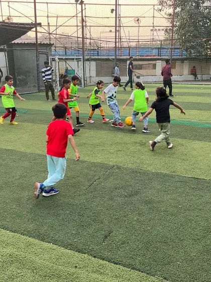 A full-field view of a kids' football match, with players in colorful bibs chasing the ball with incredible energy.