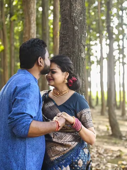 A tender moment with a kiss on the forehead. The sunlight filtering through the trees adds a warm, romantic glow to this forest maternity portrait.