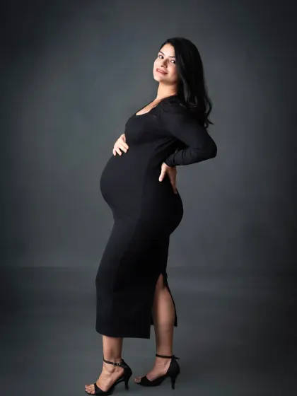 A sleek and stylish solo portrait. This mom-to-be looks incredible in a black bodycon dress and heels, showing a modern and confident side of maternity.
