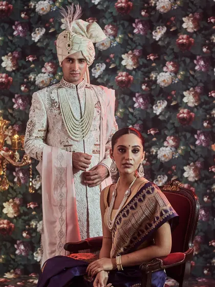 A vision of regal sophistication. Here, we present a coordinated couple's look, featuring a bride in a traditional navy blue Banarasi saree and a groom in an intricately embroidered off-white sherwani with a matching safa.