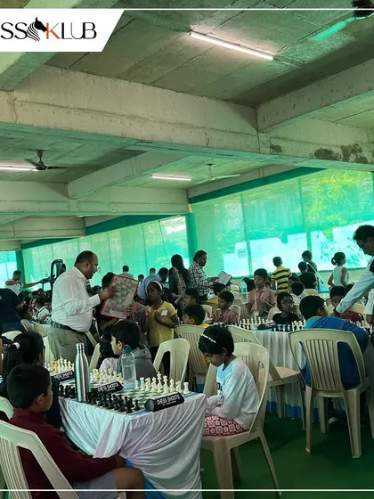 A bustling tournament hall during the Universal First Age Category Children Chess Tournament, with players and arbiters filling the space.