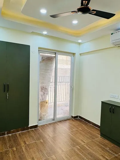 A simple bedroom layout with an olive green wardrobe and a matching low-height cabinet. The wooden flooring adds warmth to the space.
