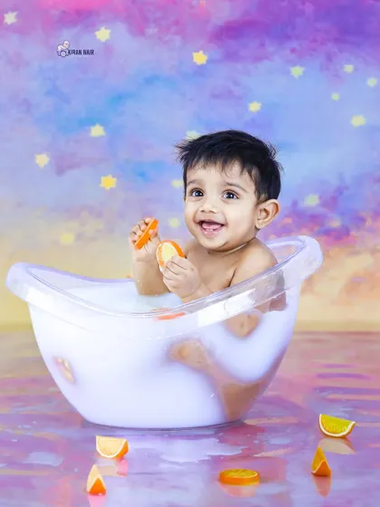 Another angle from a fun "milk bath" photoshoot. This happy toddler is playing with orange slices in the tub, set against a dreamy pastel background.
