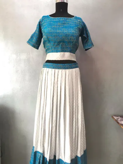 A modern take on a saree lehenga, using a simple blue and white saree. The design features a boat neck blouse and a pleated skirt with a contrasting border.
