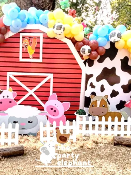 This is the main photo backdrop for the barnyard theme, featuring a big red barn, a cow-print arch, and a whole host of cute farm animals behind a white picket fence. It’s a perfect spot for birthday photos.