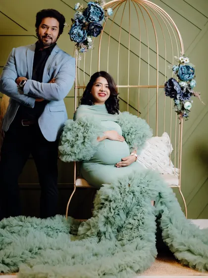 A stylish couple's shot in the studio. The mint green maternity gown provides a soft, beautiful color palette against the olive green wall and floral props.