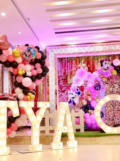 A Minnie Mouse-themed first birthday party for Nitya. The stage is decorated in pink and black, with a sequin wall and large marquee letters.