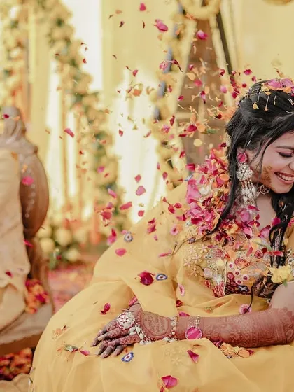 A candid shot of the bride smiling as flower petals are thrown, with the groom in the background.