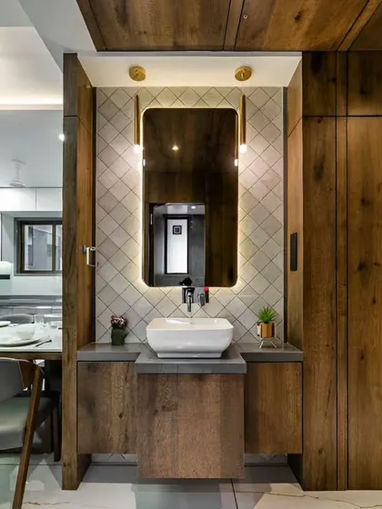 A compact washbasin area with a stylish backlit mirror and diamond-patterned tiles. The wooden vanity and ceiling panel add warmth and texture to the space.