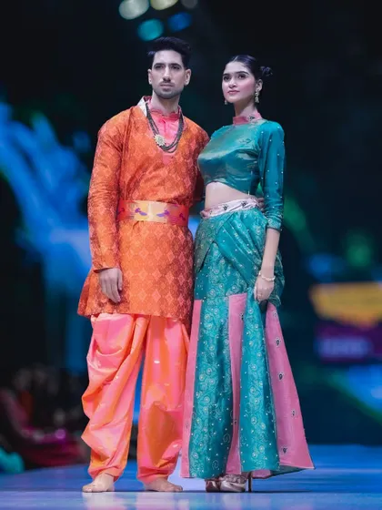 A striking pair on the runway in complementary traditional outfits. The contrast between the warm orange and cool teal creates a visually engaging photograph that highlights the versatility of the collection.