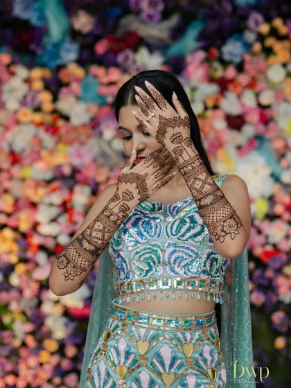 A creative pose against a floral wall, highlighting the bride's themed mehndi.