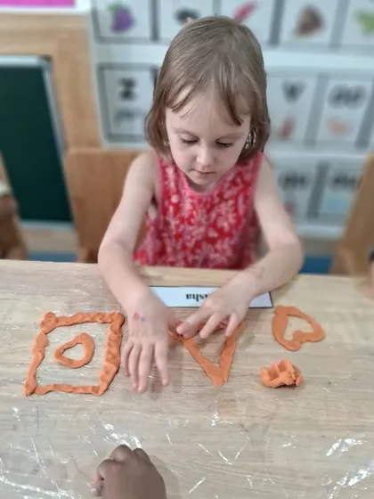 Using playdough, this girl forms different shapes like squares and hearts. This sensory activity is another way we explore geometry while strengthening hand muscles.