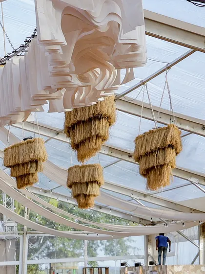 A view of the ceiling, showing the combination of the modern white fabric installation and the rustic straw chandeliers.