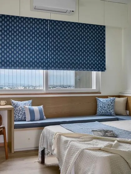 The guest room in 'Malhar' features a small study desk that transitions into a long bay window seat. The blue and white color scheme creates a fresh and calming environment for visitors.