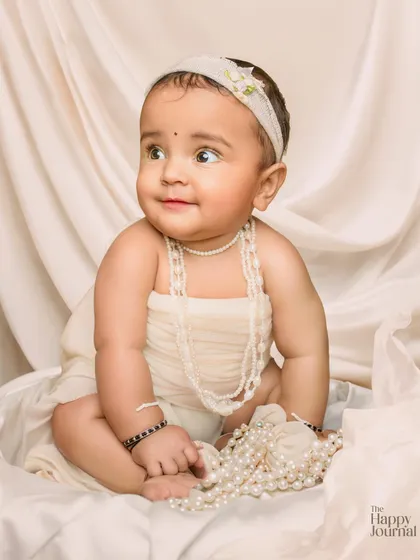 A baby girl draped in pearls, looking off to the side with a sweet smile. This creative setup is both elegant and adorable.