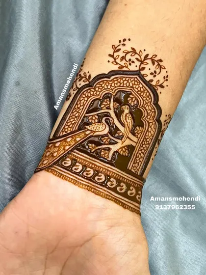 A delicate wrist cuff design featuring two birds, a peacock and a peahen, perched on a branch inside a traditional window frame.