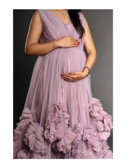 A close-up shot of a mother-to-be's torso, highlighting the beautiful texture of the ruffled lavender gown against her baby bump.
