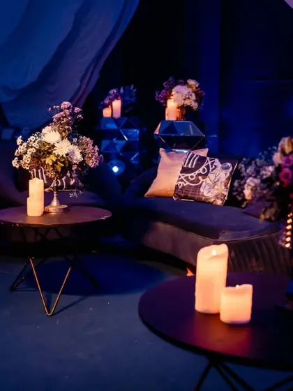 Another view of the sangeet lounge, showing plush velvet seating and floral arrangements in deep, cosmic hues, all bathed in soft candlelight.