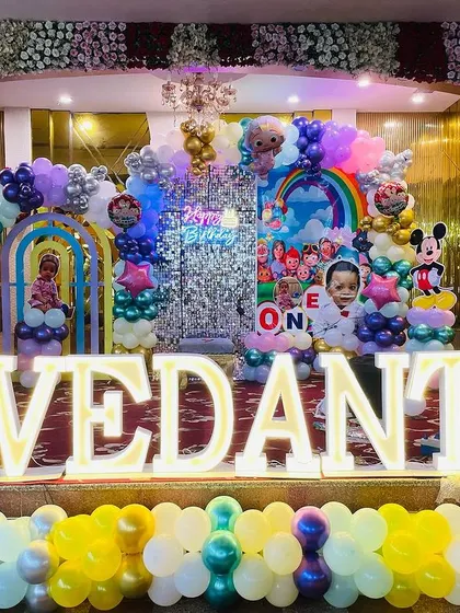 A grand, multi-themed first birthday stage. This large-scale decoration for 'Vedant' includes Cocomelon, Mickey Mouse, and other cartoon characters, with light-up letters and multiple balloon arches.