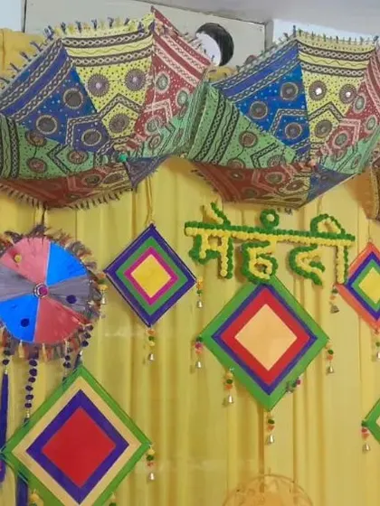 A close-up of a Mehendi backdrop featuring a yellow curtain decorated with colorful kites and Rajasthani umbrellas.