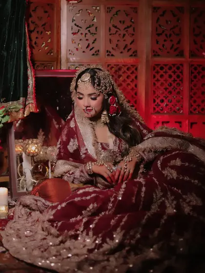 A wide shot creating a "Heeramandi" inspired scene. The bride is seated amidst candles and a decorative chest, evoking a sense of old-world royalty and romance.
