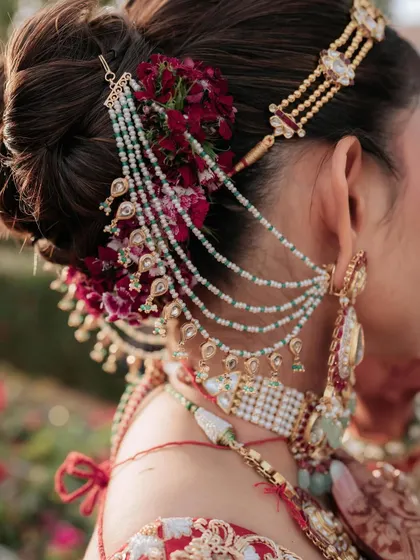 A close up of an intricate bridal bun, adorned with deep red flowers and a multi-layered hair accessory. I focus on creating these detailed updos that not only look stunning but also securely hold the dupatta and jewelry in place.