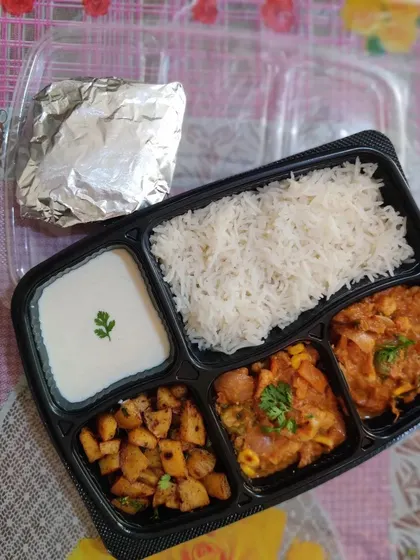 A healthy and balanced meal box with rotis, jeera rice, a mixed vegetable corn curry, a dry potato sabzi, and fresh homemade curd.