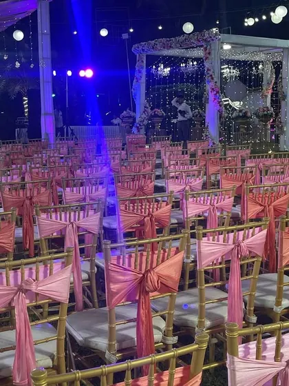 Rows of elegantly decorated chairs ready for guests at a wedding reception. The pink sashes add a pop of color and tie the seating in with the overall theme.