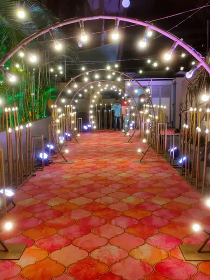 A modern and stylish entrance walkway made of semi-circular metal arches. The path is lit with large globe bulbs and uplighting for a dramatic effect.