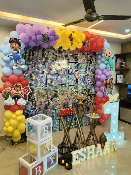 A vibrant Cocomelon themed first birthday party, complete with a colorful balloon arch, a silver shimmer wall, and cutouts of all the favorite characters.